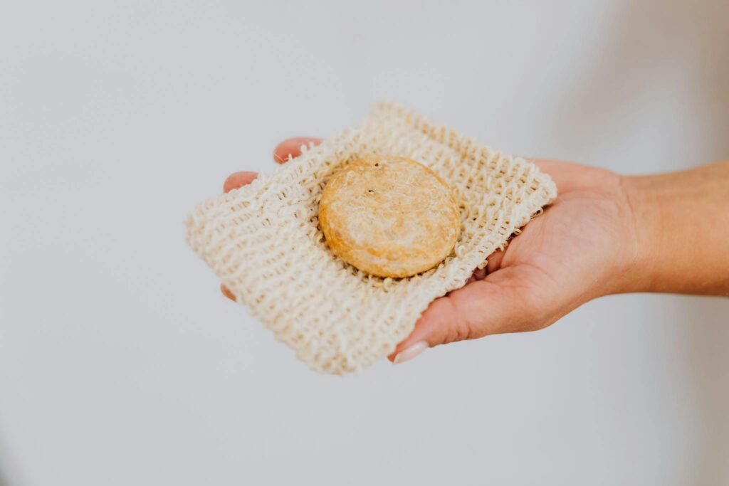 A hand holding eco-friendly handmade soap on a natural loofah pad, promoting sustainable skincare.
