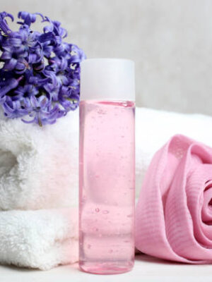Pink shower gel, washcloth and terry towel on a neutral background.