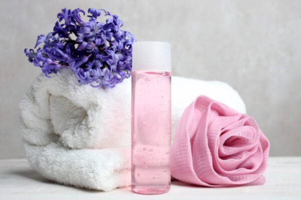 Pink shower gel, washcloth and terry towel on a neutral background.